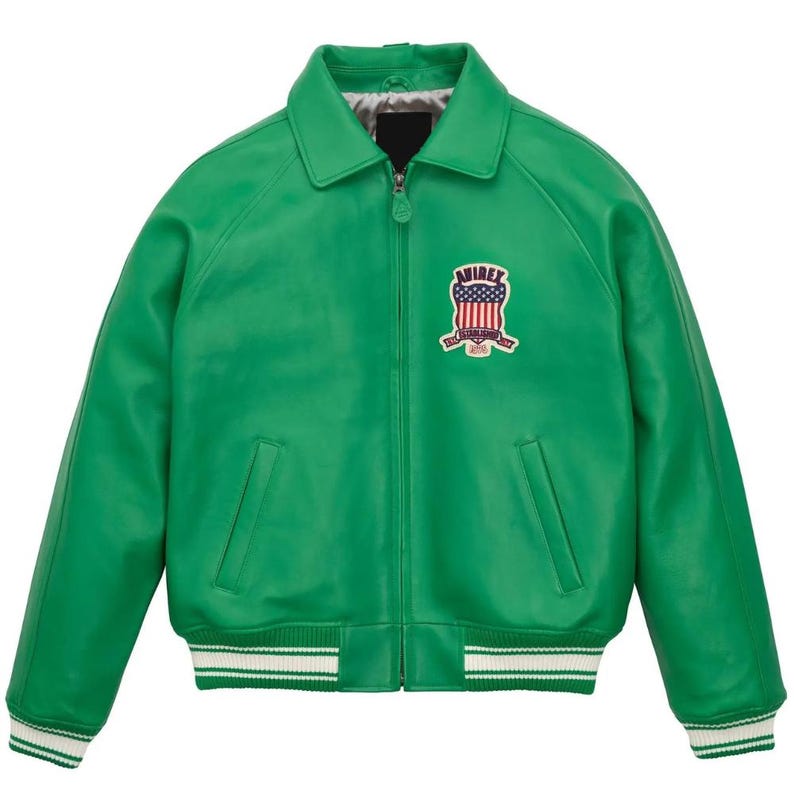 Puede incluir: Chaqueta de cuero verde brillante con cuello y cierre de cremallera. Cuenta con un parche en el pecho con el texto "AVIREX" y un dise&ntilde;o con la bandera estadounidense. Los pu&ntilde;os y el dobladillo tienen detalles a rayas blancas y verdes. Mide unos 76 cm de largo.