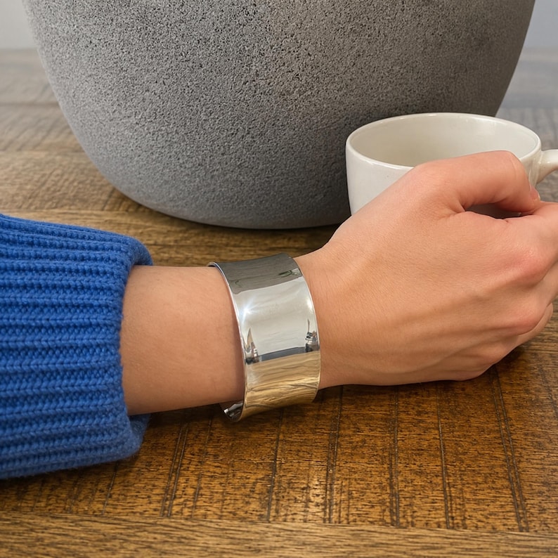Modern 925 sterling silver wide cuff bracelet with a sleek polished finish and bold minimalist design. This chunky silver arm cuff features an open adjustable style for a comfortable fit, making it perfect for everyday wear or special occasions. The reflective statement bangle adds contemporary elegance to any outfit and pairs beautifully with casual or dressy looks. A timeless silver cuff bracelet for women and a thoughtful gift for birthdays, anniversaries, or holidays.