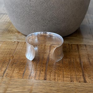 Modern 925 sterling silver wide cuff bracelet with a sleek polished finish and bold minimalist design. This chunky silver arm cuff features an open adjustable style for a comfortable fit, making it perfect for everyday wear or special occasions. The reflective statement bangle adds contemporary elegance to any outfit and pairs beautifully with casual or dressy looks. A timeless silver cuff bracelet for women and a thoughtful gift for birthdays, anniversaries, or holidays.