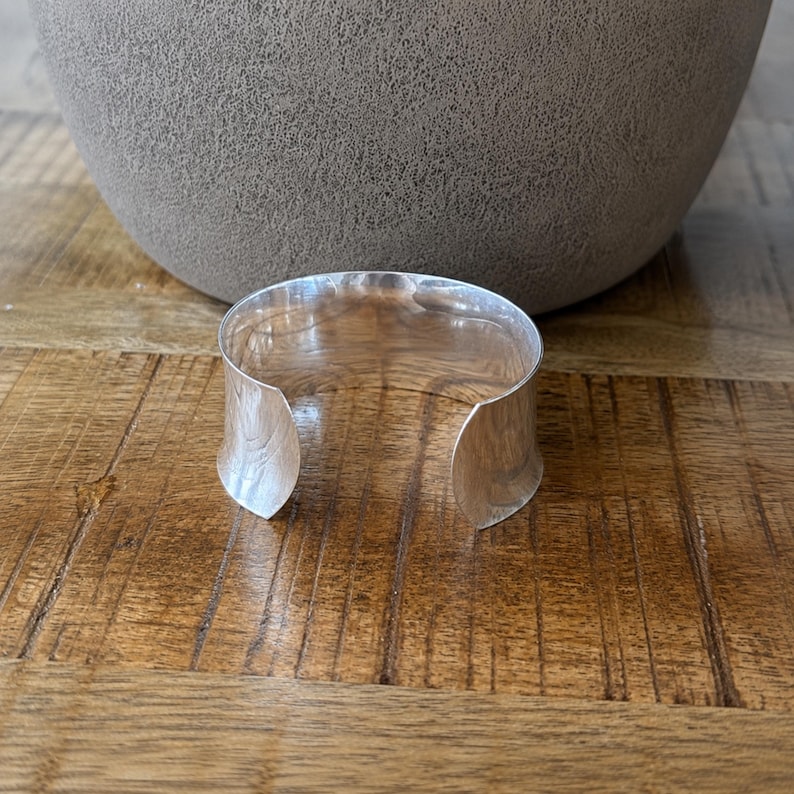 Modern 925 sterling silver wide cuff bracelet with a sleek polished finish and bold minimalist design. This chunky silver arm cuff features an open adjustable style for a comfortable fit, making it perfect for everyday wear or special occasions. The reflective statement bangle adds contemporary elegance to any outfit and pairs beautifully with casual or dressy looks. A timeless silver cuff bracelet for women and a thoughtful gift for birthdays, anniversaries, or holidays.