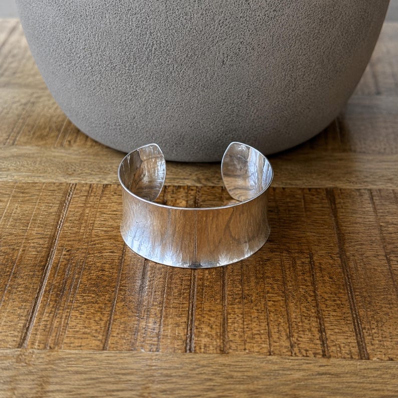 Modern 925 sterling silver wide cuff bracelet with a sleek polished finish and bold minimalist design. This chunky silver arm cuff features an open adjustable style for a comfortable fit, making it perfect for everyday wear or special occasions. The reflective statement bangle adds contemporary elegance to any outfit and pairs beautifully with casual or dressy looks. A timeless silver cuff bracelet for women and a thoughtful gift for birthdays, anniversaries, or holidays.