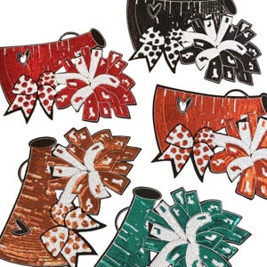 May include: A collection of sequined cheerleading megaphones and pom-poms in various colors, including red, black, brown, and green. Each megaphone has a heart-shaped cutout. The pom-poms feature a mix of solid and patterned designs.