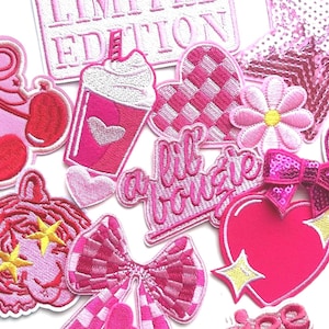 May include: A collection of pink embroidered patches in various shapes, including cherries, hearts, bows, and a flower. Some patches feature text like "Limited Edition" and "Lil Boujee". The patches are in shades of pink with white and yellow accents.