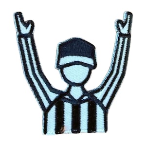 May include: Embroidered patch featuring a referee in a black and white striped uniform, arms raised in a signal. The patch has a black cap and a light blue background. The design is a stylized representation of a sports official.