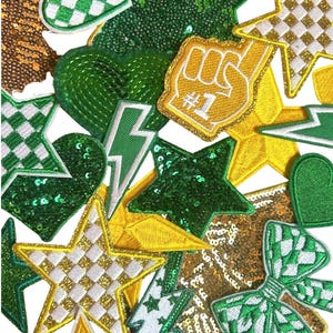 May include: A collection of assorted patches in various shapes, including stars, hearts, and lightning bolts. The patches feature green, gold, and white colors, with sequin and checkered patterns. One patch displays a foam finger with the number one.