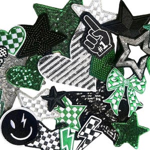 May include: A collection of decorative patches in various shapes, including stars, hearts, bows, and lightning bolts. The patches feature a mix of black, white, and green colors, with sequin and checkered patterns. One patch displays a smiley face and another shows a hand with the number one.