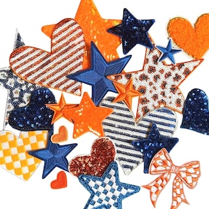 May include: A collection of decorative patches in various shapes, including stars, hearts, and a bow. The patches feature a mix of textures, such as sequins, stripes, and checkered patterns. Colors include orange, blue, white, and red.