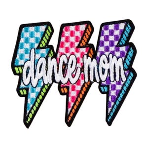 May include: Embroidered patch featuring three lightning bolt shapes in blue, pink, and purple, each with a checkered pattern. The words "dance mom" are embroidered in white across the bolts. The patch has a black border and is designed for apparel.
