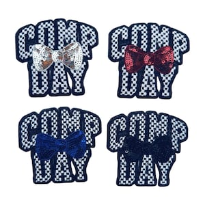 May include: Four patches with the text "COMP DAY" in a black and white checkered pattern. Each patch has a sequined bow in silver, red, blue, and black. These patches are suitable for clothing or accessories.