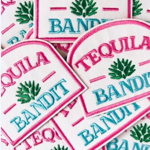 May include: A collection of embroidered patches with the words "TEQUILA BANDIT" in pink and teal. The patches feature a white background with a pink border and a green agave plant design.