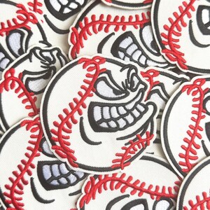 May include: A collection of baseball-themed patches. Each patch features a white baseball with red stitching and a grinning face with black outlines. The patches are scattered across a surface.