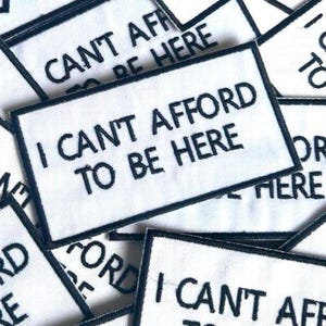 May include: White rectangular patches with black borders and the embroidered text "I CAN'T AFFORD TO BE HERE". The patches are scattered, with some overlapping. The text is in a bold, sans-serif font.
