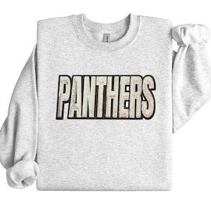 May include: A light gray sweatshirt with the word "PANTHERS" in a distressed, textured font across the chest. The text is outlined in black. The sleeves are long and cuffed at the wrists.
