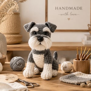 May include: A handcrafted crochet Schnauzer dog figurine featuring a dark gray and white yarn color scheme, pointed ears, and a textured beard. The plush toy is positioned on a wooden surface surrounded by various balls of yarn and crochet tools.