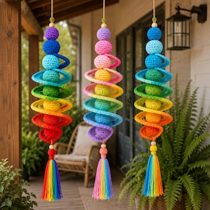 May include: Three hanging crochet wind spinners featuring a vertical arrangement of colorful spheres and spiral elements. Each piece displays a spectrum of vibrant hues including red, orange, yellow, green, blue, and purple, finished with a rainbow tassel.