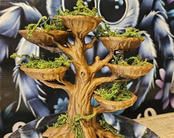 May include: A brown, tree-shaped display stand with five circular, bowl-like platforms extending from the trunk. Each platform is filled with bright green, textured moss. The structure features a detailed, textured bark finish and a wide, root-like base.