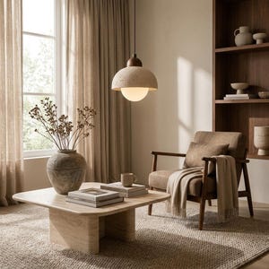 May include: A pendant light featuring a textured beige dome shade with a dark wood top and a spherical white glass bulb. The fixture hangs from a thin black cord, providing illumination in a room with a stone coffee table and an armchair.