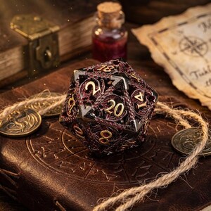 Puede incluir: Un dado de múltiples caras con un diseño rojo y negro, con numeración dorada. El dado está sobre un libro encuadernado en cuero, con monedas y una pequeña botella en el fondo, lo que sugiere un tema de juego de fantasía o de mesa.