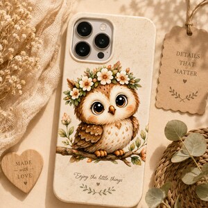 May include: A cream-colored phone case featuring a brown owl with large eyes wearing a floral crown while perched on a branch. The text "Enjoy the little things" is printed below the owl, accompanied by a small heart and leaf graphic.