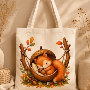 May include: A cream-colored canvas tote bag featuring a printed illustration of a small orange squirrel sleeping inside a large acorn shell. The squirrel is curled up holding a tiny nut, surrounded by autumn leaves, berries, and tree branches.