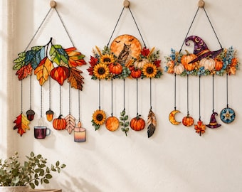 May include: Three decorative wall hangings featuring stained glass-style designs. The left shows autumn leaves, acorns, a mug, and a candle. The centre features an owl, sunflowers, and pumpkins. The right displays a witch hat, pumpkins, and a moon.