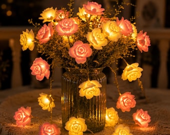 May include: A string of LED lights shaped like roses, with pink and yellow illuminated flower heads. The lights are arranged in a vase with a bouquet of flowers, creating a warm, inviting ambiance. The rose lights are perfect for home decor.