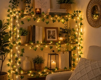 May include: A wooden shelving unit decorated with strings of artificial ivy and warm white fairy lights. The shelves hold various potted plants, books, framed art, a black metal lantern with a white pillar candle, and a ceramic vase.