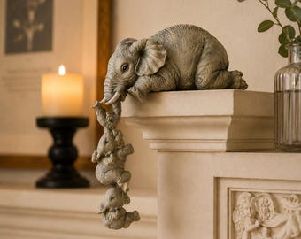 May include: A grey elephant ornament with three smaller elephants suspended from its trunk. The elephant rests on a white ledge. The ornament is a decorative item.