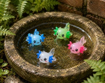 May include: Four small, translucent axolotl figurines in blue, green, pink, and white with blue accents. Each figurine features a cartoonish face with black eyes, a small mouth, and external gills, floating in a circular stone basin filled with water.