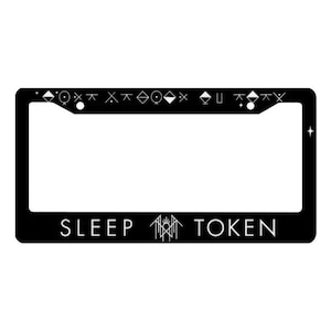 May include: Black license plate frame with white text that reads "SLEEP TOKEN". The top border features a series of geometric symbols. A star is in the right corner. The frame is rectangular.