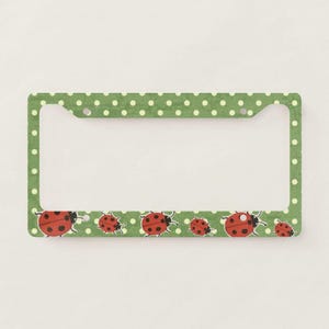 May include: A rectangular license plate frame featuring a green background with a white polka dot pattern. The bottom section of the frame is decorated with a series of red ladybugs with black spots arranged in a horizontal row across the surface.