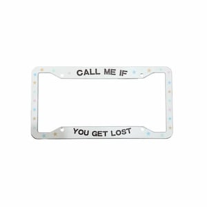 May include: A white rectangular license plate frame featuring the text CALL ME IF YOU GET LOST in dark lettering. The frame is decorated with small, multicolored pastel stars scattered along the border, including blue, pink, and yellow hues.