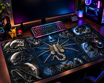 May include: A rectangular desk mat featuring a collage of Alien franchise imagery, including multiple Xenomorph heads and a central facehugger on a dark blue background. The mat is positioned on a wooden desk surface under a computer monitor.