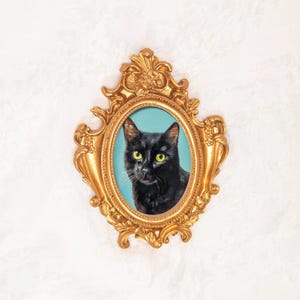 Puede incluir: Un retrato de un gato negro con ojos de color amarillo brillante sobre un fondo azul claro sólido, encerrado en un marco dorado ovalado y ornamentado que presenta intrincados adornos y detalles florales en los bordes superior e inferior.