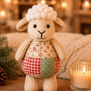 Könnte beinhalten: Ein Plüschschaf mit cremefarbenem, strukturiertem Körper, Schlappohren und einem Kopf mit weißen Bommeln. Der Rumpf ist im Patchwork-Stil gestaltet und zeigt florale Muster, rot-weißes Vichy-Karo sowie grüne Stoffe mit weißen Punkten.