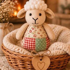 Pu&ograve; includere: Un peluche a forma di pecora con testa fatta di pompon bianchi, braccia in maglia beige e corpo patchwork con motivi a quadretti rossi, pois verdi e fiori. Il giocattolo &egrave; posizionato in un cesto di vimini marrone foderato in tessuto color crema.