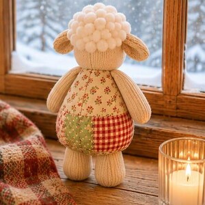 Pu&ograve; includere: Un peluche a forma di pecora con testa fatta di pon pon bianchi, braccia e gambe in tessuto a coste beige e un busto caratterizzato da un design patchwork con tessuto floreale, tessuto verde fantasia e un motivo a quadri rossi e bianchi.