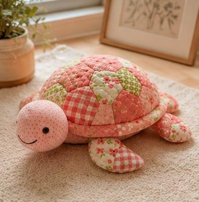 May include: A plush turtle toy featuring a quilted shell made of various fabric patches in shades of pink, white, and green with floral and gingham patterns. The head is light pink with small black eyes and a stitched smile, and the limbs match.
