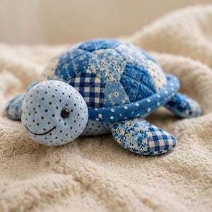May include: A stuffed turtle toy crafted from various blue and white fabric patches. The shell features a quilted patchwork design with floral, gingham, and polka dot patterns. The head is light blue with small black polka dots and a stitched smile.