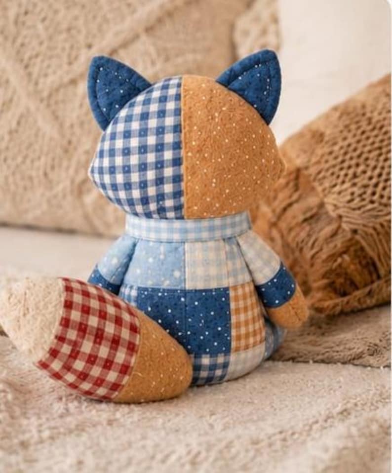 May include: A patchwork fox plush toy in various fabrics. The fox has blue and white gingham, dotted tan, and a red and white checked tail. The toy is on a soft, textured surface. A charming handmade item.