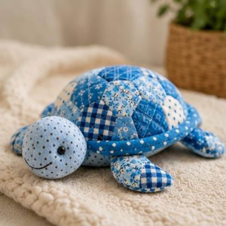 May include: A stuffed turtle toy featuring a patchwork shell made of various blue and white patterned fabrics, including gingham, floral, and polka dot prints. The head is light blue with small black polka dots, a stitched smile, and black bead eyes.
