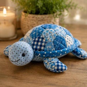 May include: A stuffed turtle toy crafted from various blue and white fabric patches. The shell features a quilted pattern with floral, gingham, and polka dot prints. The head is light blue with small black polka dots and a stitched black smile.