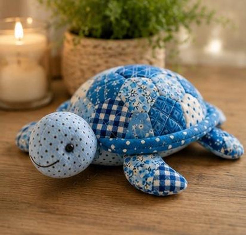 May include: A stuffed turtle toy crafted from various blue and white fabric patches. The shell features a quilted pattern with floral, gingham, and polka dot prints. The head is light blue with small black polka dots and a stitched black smile.