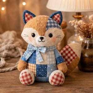 May include: A handmade fox plush toy with a patchwork design. The fox has a brown and white spotted face, blue and red plaid ears, and a blue bow tie. The body is a mix of blue, white, and tan fabrics. The fox's paws are red and white checkered. The toy is on a wooden surface.