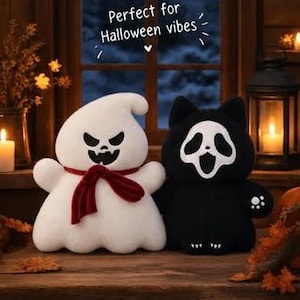 May include: A white plush ghost with a black jagged face and a red velvet scarf next to a black plush cat wearing a white ghost mask with a wide open mouth. The text above reads Perfect for Halloween vibes with a small heart icon below the text.