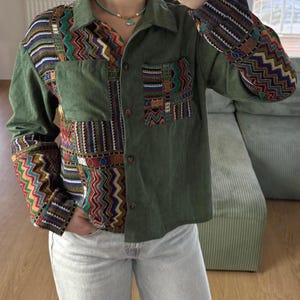 Peut inclure: Chemise en velours côtelé vert olive avec des manches et des empiècements à motifs colorés. La chemise a une fermeture boutonnée, deux poches et un col. Les manches et les panneaux avant présentent des motifs géométriques.
