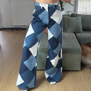 Könnte beinhalten: Weit geschnittene Jeans mit Patchwork-Design. Die Jeans hat ein geometrisches Muster aus blauen und weißen Rauten. Die hoch taillierte Hose hat einen Knopf- und Reißverschluss und einen klassischen Fünf-Taschen-Stil.
