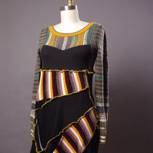 May include: A black long-sleeved dress with a patchwork design. The dress features a variety of colorful stripes and patterns, including yellow, red, white, and brown. The dress has a scoop neckline and a relaxed fit.