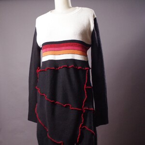 May include: A long-sleeved black and white striped sweater dress with a red, orange, and pink stripe detail. The dress has a ruffled hemline with red stitching.