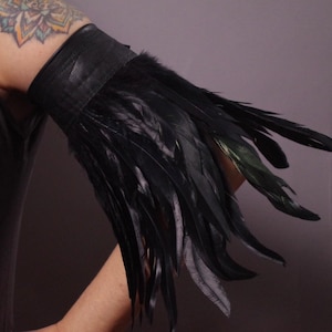 May include: A black leather arm cuff with a long fringe of black feathers.